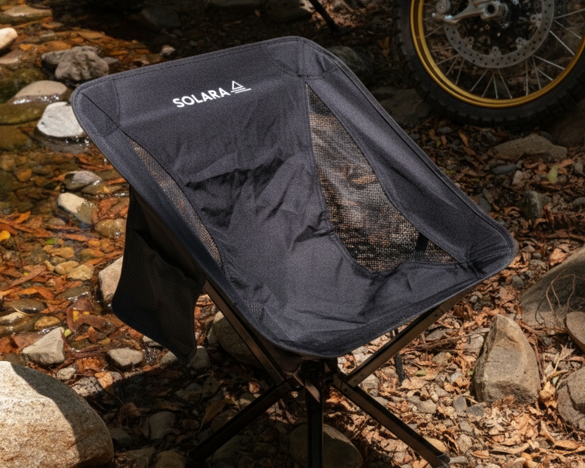 Black camping chair with 'Solara' branding on a rocky ground with a motorcycle in the background.