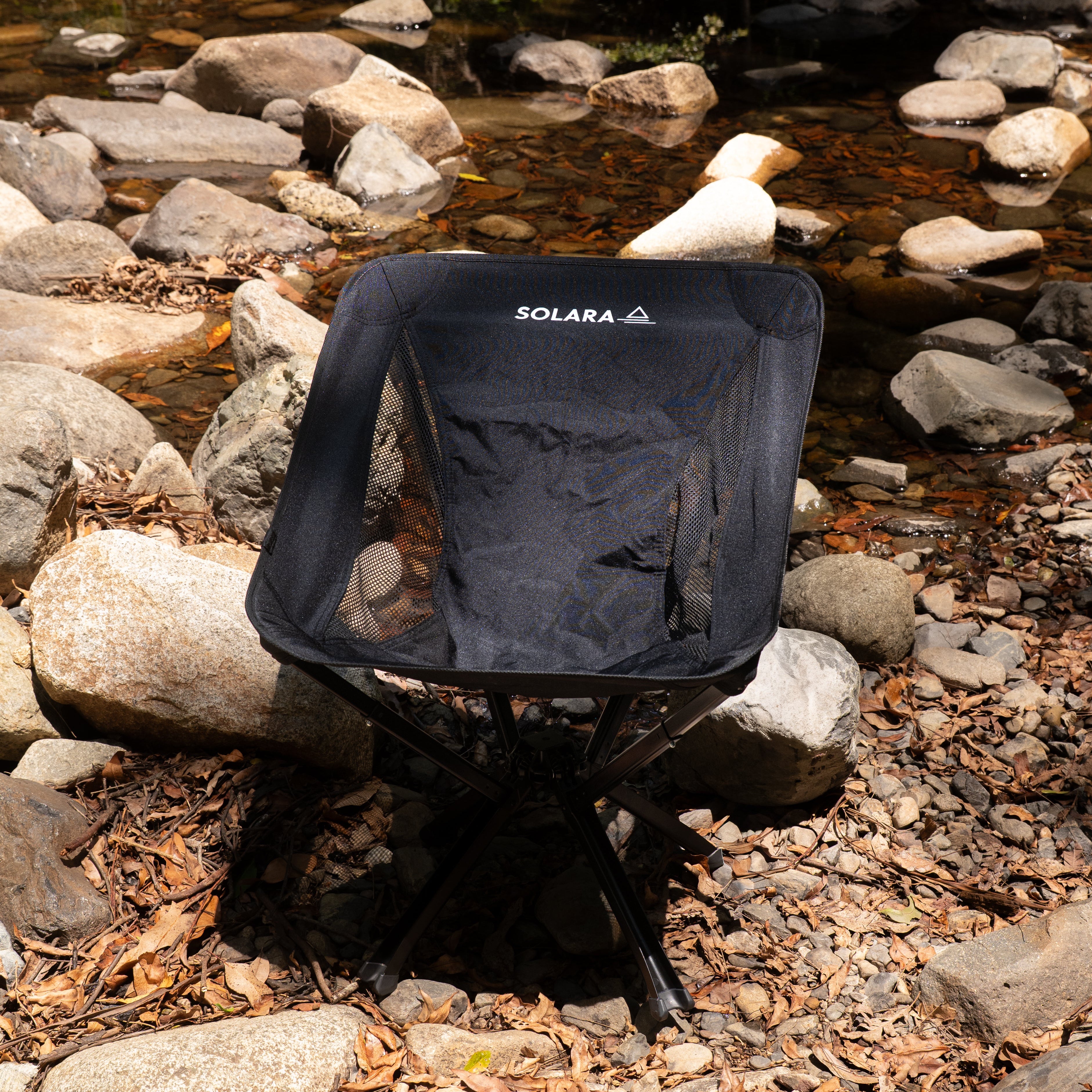 Black camping chair with 'Solara' branding on a rocky stream bank