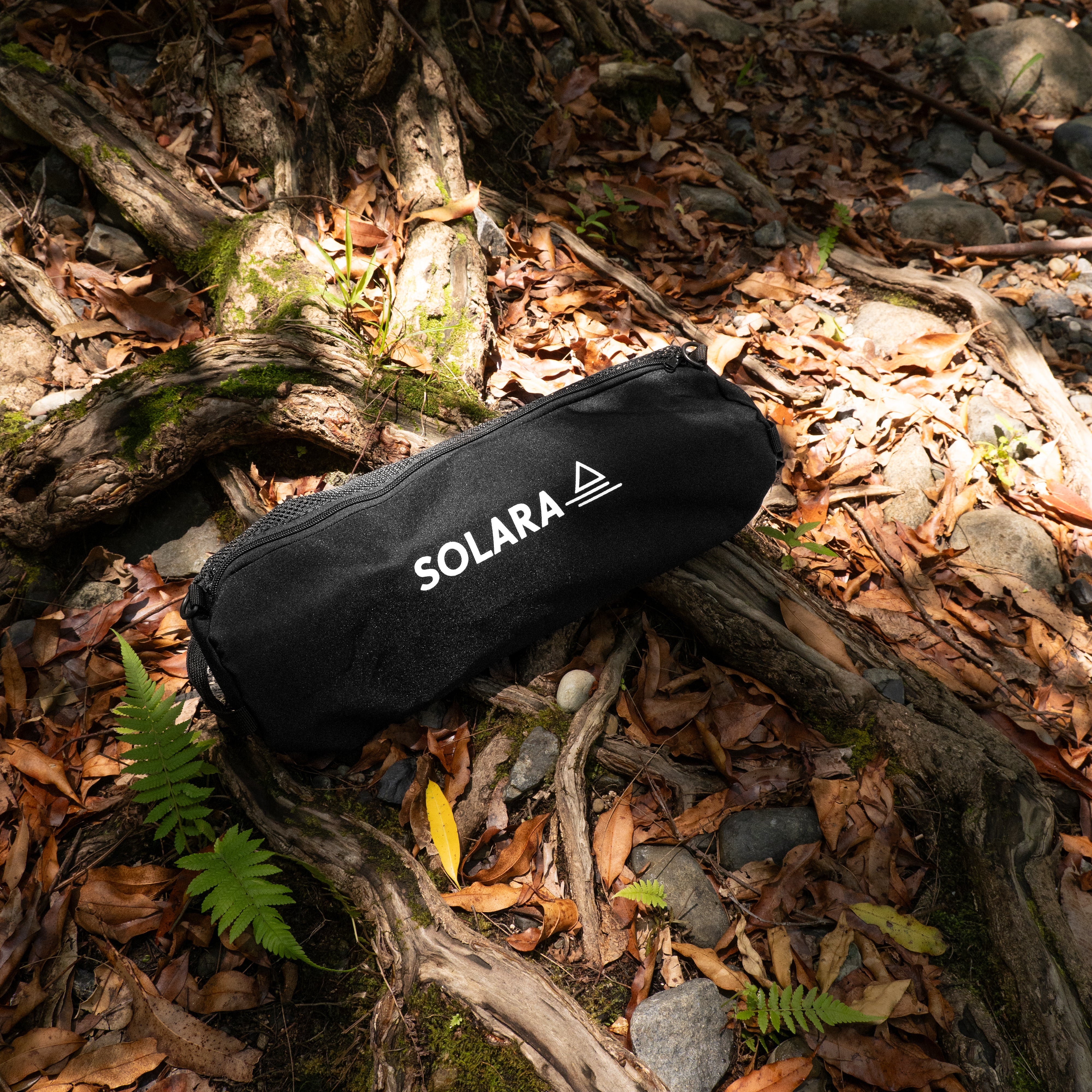Black cylindrical pouch with 'SOLARA' branding on a forest floor.