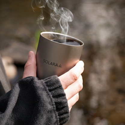 Hand holding a Solara mug with steam against a natural background