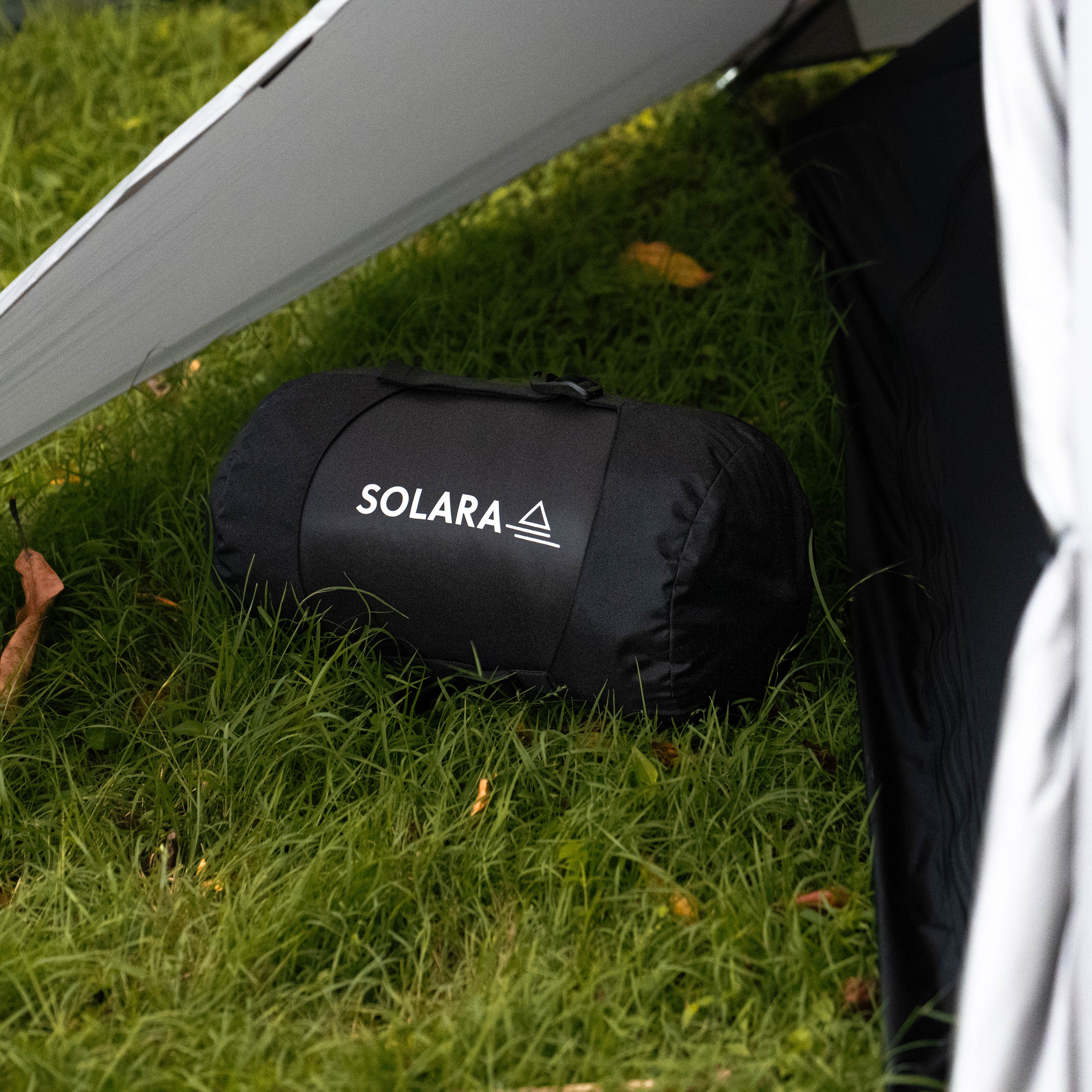 Roll-up sleeping bag labeled 'SOLARA' on grass next to a tent