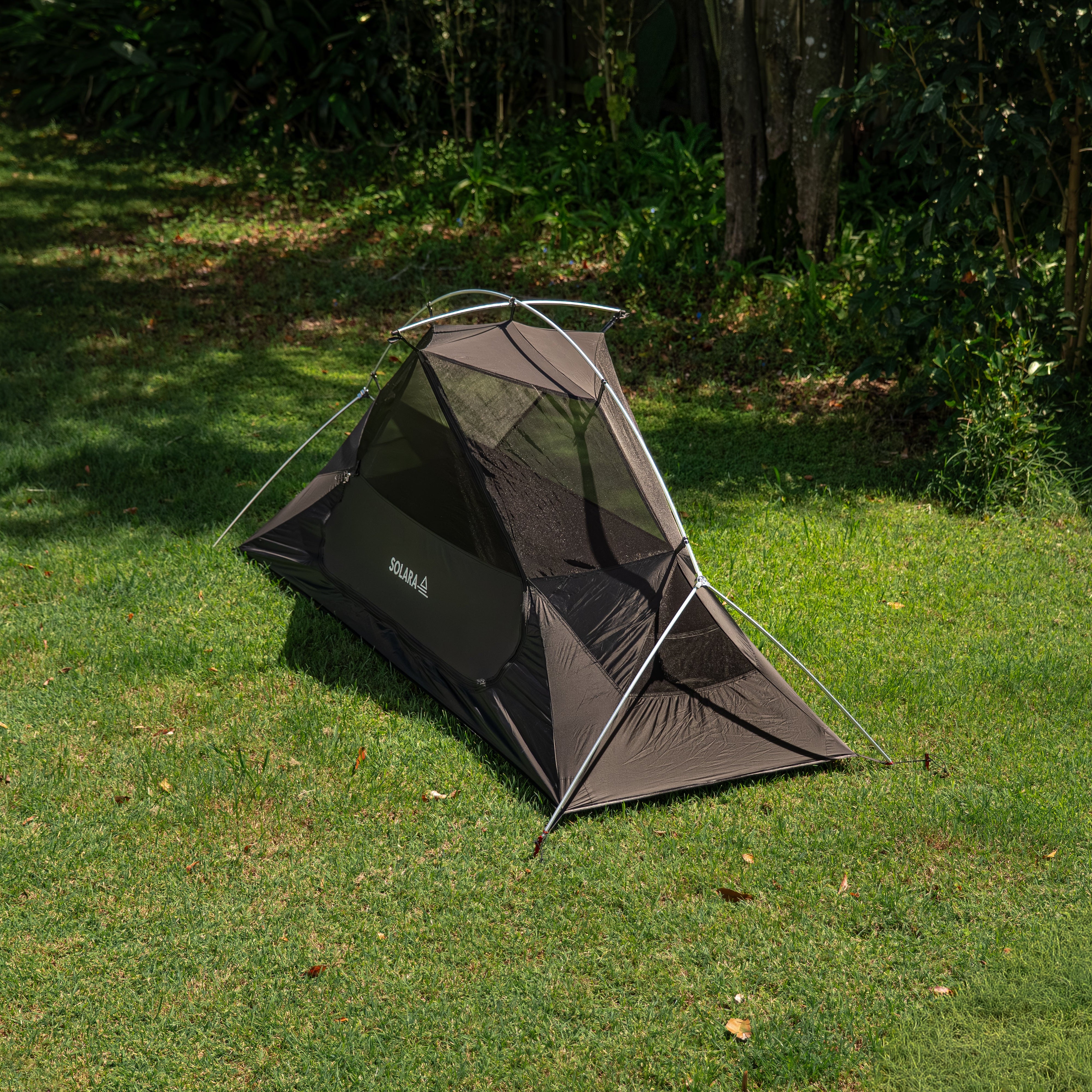 Black camping tent on grass with trees in the background