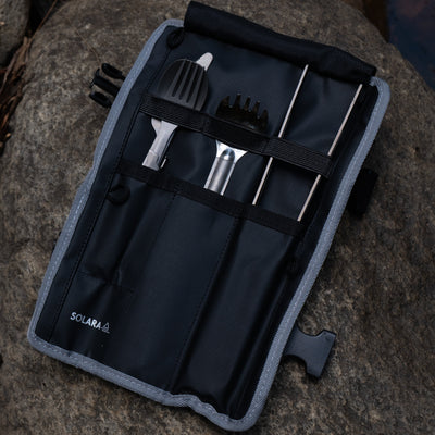 Set of barbecue tools in a black and gray carrying case on a rocky surface