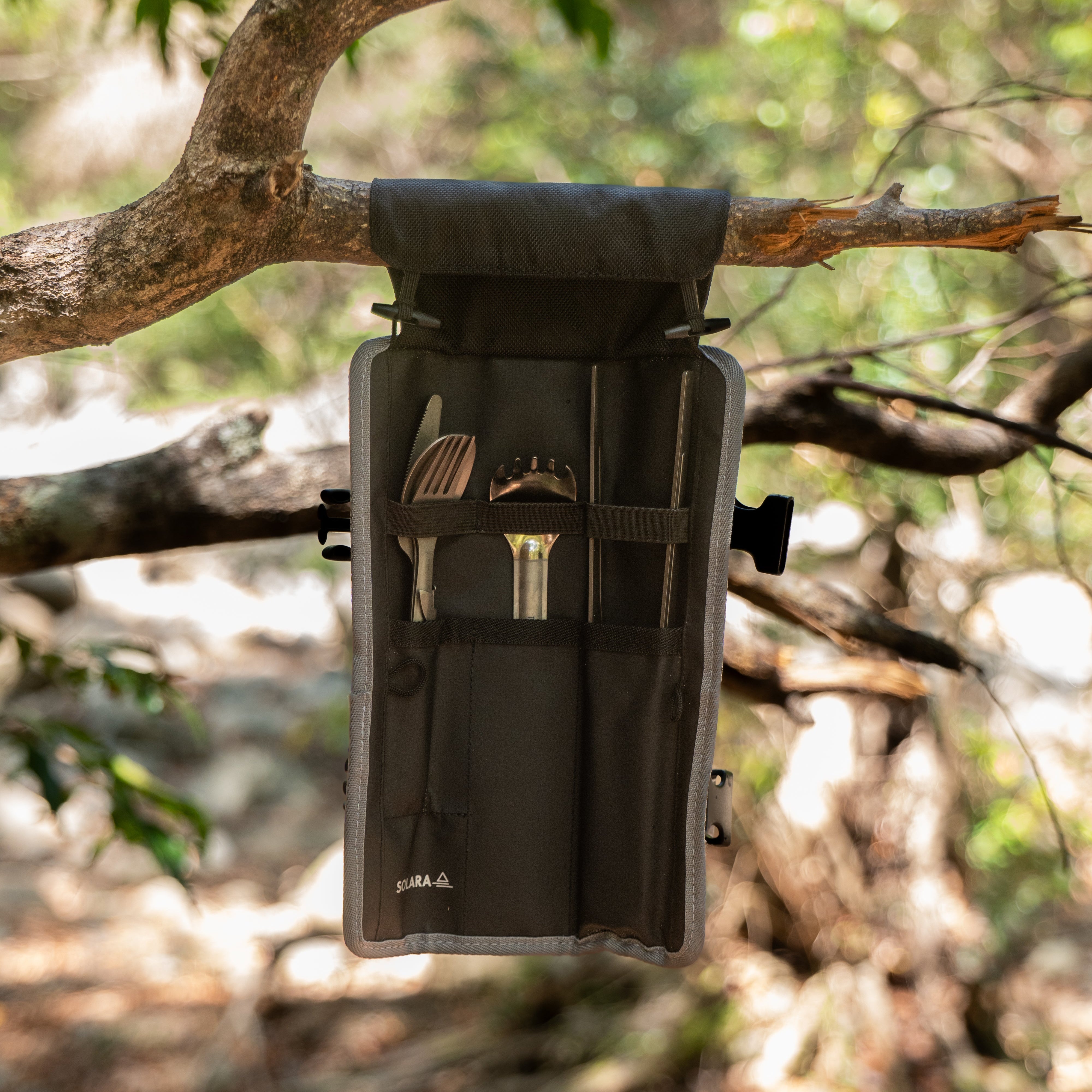 Black tool pouch with utensils hanging from a tree branch in a forest setting