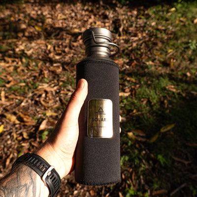 Person holding a black insulated water bottle with a logo in a natural setting